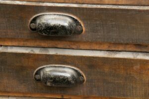 Close-up of a dark wood drawer front with black steel bin pull showing surface wear and staining.