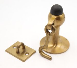 Brushed brass wall-mounted door stopper with a black rubber tip and attached latch hook, shown in a close-up view.