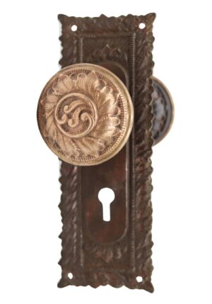 Victorian passage door knob set with an ornate back plate, a brass front knob, and visible keyhole cutout.