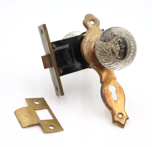 Traditional passage door knob set with clear swirl glass knobs, antique brass back plates, a mortise lock, and a strike plate.