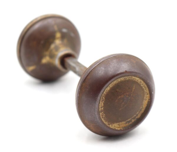 Pair of vintage passage door knobs with an attached spindle, shown in a close-up view with heavy surface wear on the antique bronze finish.