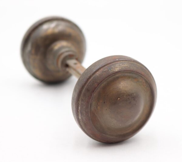 Pair of vintage passage door knobs with concentric detailing and a spindle, shown in an antique bronze finish with visible surface wear.