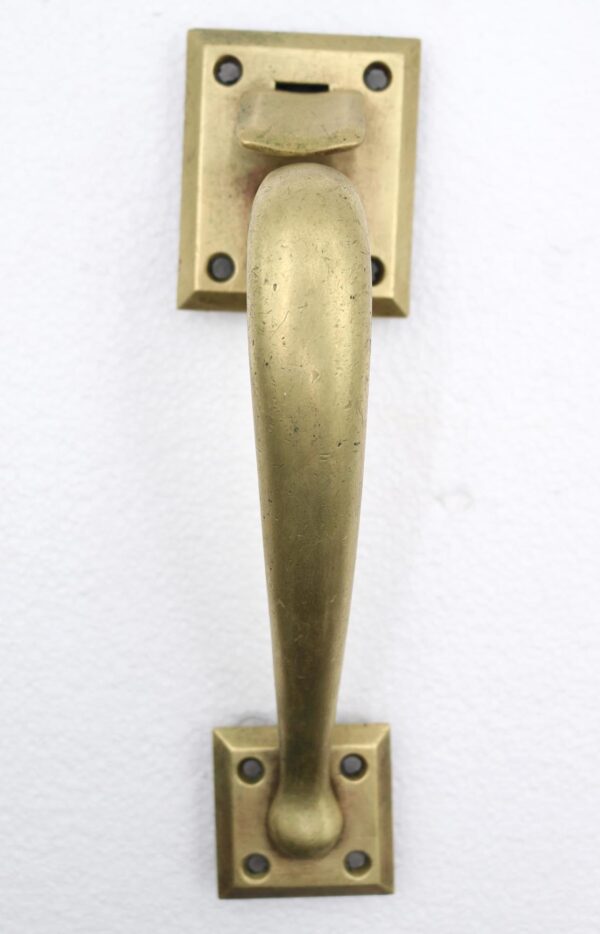 Vintage brass door pull with a curved handle and square plates.