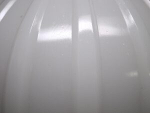 Close-up of a white milk glass pendant light shade with fluted vertical ridges and a glossy surface.