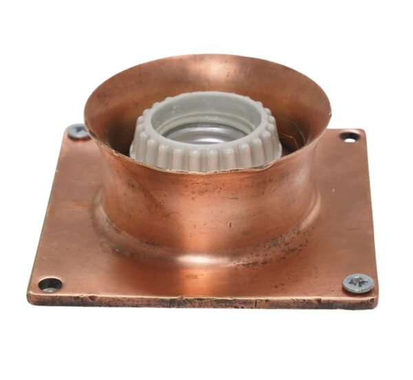 Copper-finish brass flush mount light with a square base and central bulb socket holder, shown in close-up with visible surface wear.