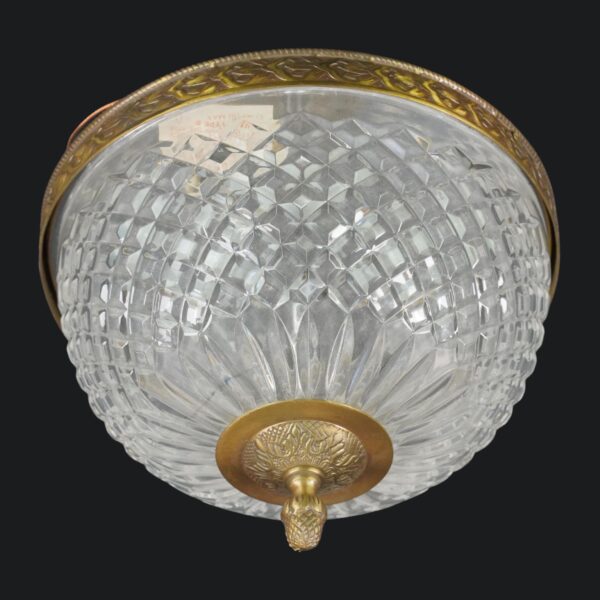 Crystal flush mount light with a faceted clear shade, ornate brass rim, and pineapple finial viewed from below.