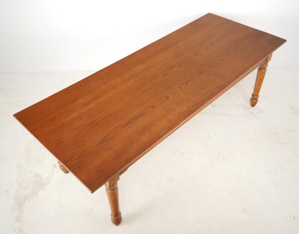 Farmhouse dining table with a medium wood tone top and turned wooden legs, shown at an angle.