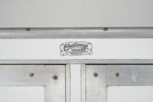 Close-up of a white icebox refrigerator showing the Challenge badge, metal trim, and worn door panels with visible latch hardware and surface wear.