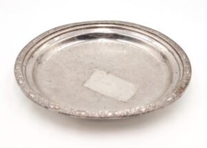 Art Deco round platter with an engraved rim, shown from above with visible wear and scuffs on the surface.