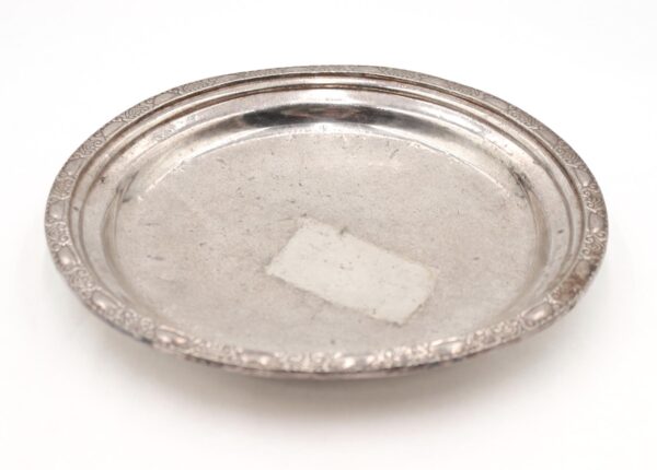 Art Deco round platter with an engraved rim, shown from above with visible wear and scuffs on the surface.
