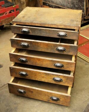 Vintage industrial workshop chest with five drawers, one open to show a divider, dark wood tone with black steel bin pulls and heavy surface wear.