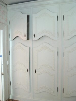 White built-in cabinets with curved French-style doors, decorative floral motifs, and original hardware fill the frame.