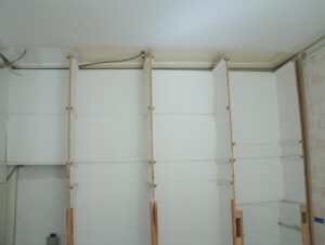 Disassembled built-in cabinet bank with white French curve doors and visible wood framing, showing multiple upper and lower cabinet sections in a row.
