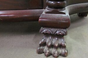 Close-up of the cabinet’s carved wood foot, showing claw feet and decorative trim in a dark wood tone.