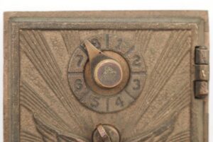Close-up of a vintage post office box door with a combination dial and flying eagle relief, showing the right edge hinge and aged bronze finish.