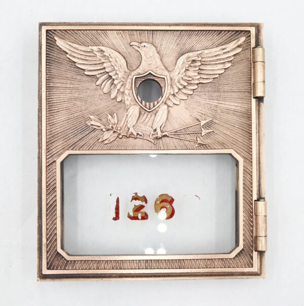 Brass post office box door with a flying eagle design, an attached glass panel, and the number 126 visible behind the glass.