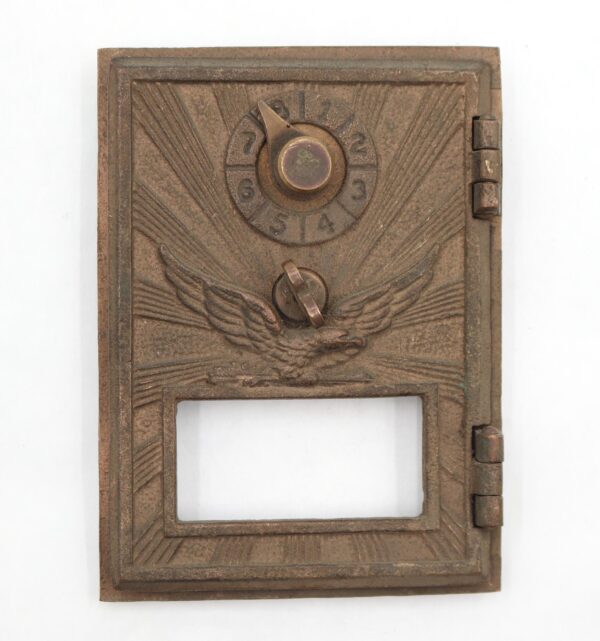 Vintage bronze post office box door with a combination dial, flying eagle relief, and a rectangular window opening.