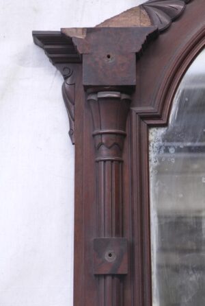 Close-up of the top corner of a Victorian hall mirror in a dark wood tone, showing carved geometric pillar detailing and part of the original mirror glass.