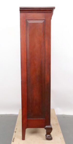Tall mahogany cabinet with a paneled front, decorative top molding, and a carved foot at the base, shown in a straight-on view.