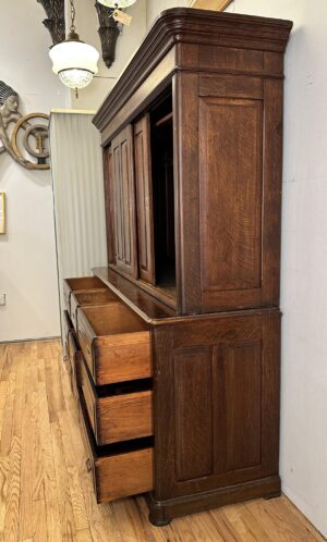 Dark wood cabinet with a tall upper section, two sliding doors, and several open drawers below, shown at an angle.