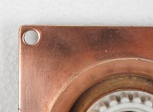 Close-up of a copper-finish brass flush mount light showing the mounting plate with a corner hole and part of the exposed bulb ring.