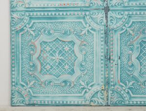 Blue ornate tin wall panel with raised four-quadrant decorative pattern and a weathered vertical seam down the center.