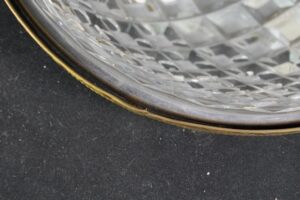 Close-up of a crystal flush mount light showing the clear faceted glass and polished brass rim with visible wear along the edge.