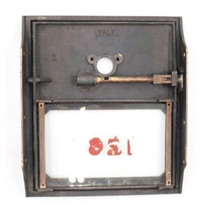 Vintage brass Yale post office box door with attached glass panel, keyhole opening, and visible latch mechanism.