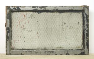 Rectangular reclaimed window with a worn wood frame and clear chicken wire glass pane, showing chipped paint and rusted surface wear.