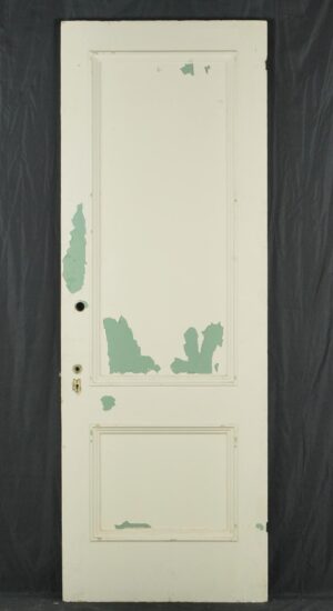 Vintage white wooden privacy door with two panels, showing original brass hardware and chipped paint from prior use.