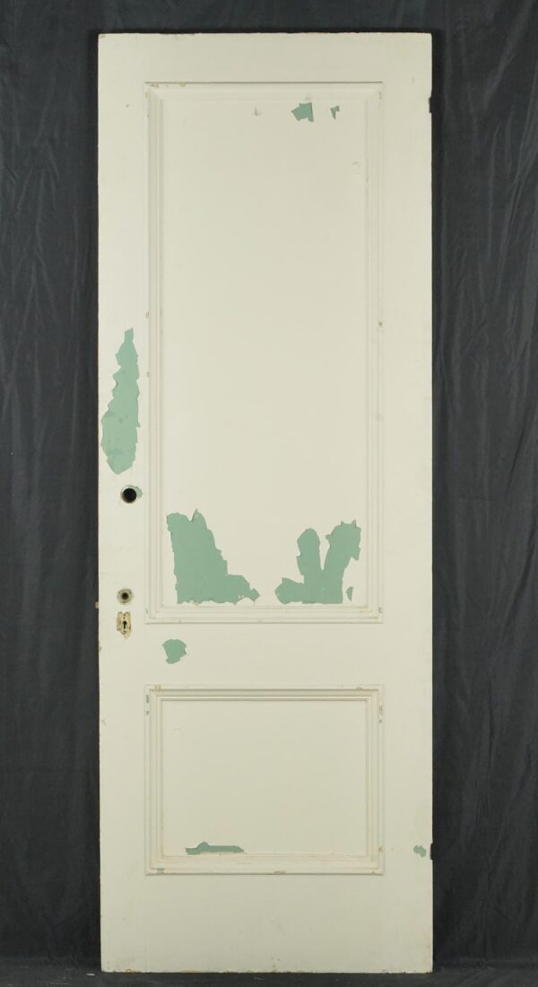 Vintage white wooden privacy door with two panels, showing original brass hardware and chipped paint from prior use.