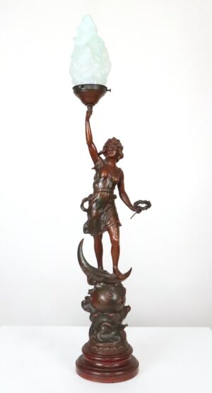 Art Nouveau wood table lamp with a woman balancing on a crescent moon and holding a flame-shaped glass torch shade.