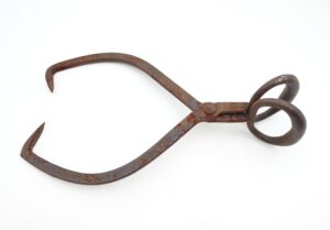 Antique wrought iron ice tongs with hooked gripping ends and circular handles, shown in a single side view with heavy surface wear and rust.