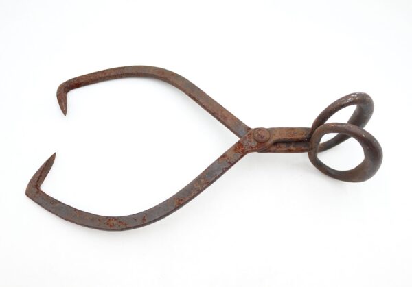 Antique wrought iron ice tongs with hooked gripping ends and circular handles, shown in a single side view with heavy surface wear and rust.