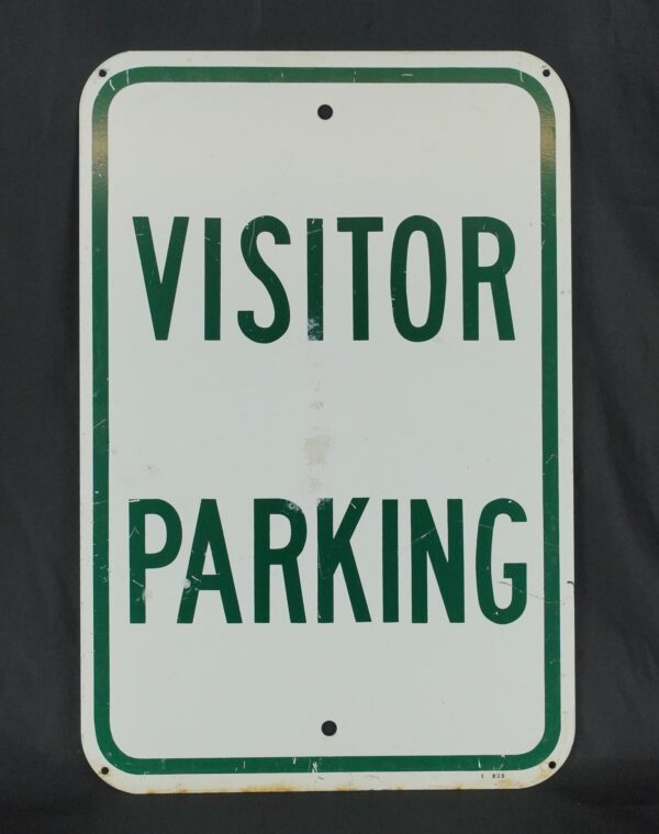 Steel visitor parking traffic sign with green and white enamel finish, rounded corners, two predrilled mounting holes, and visible surface wear and stains.