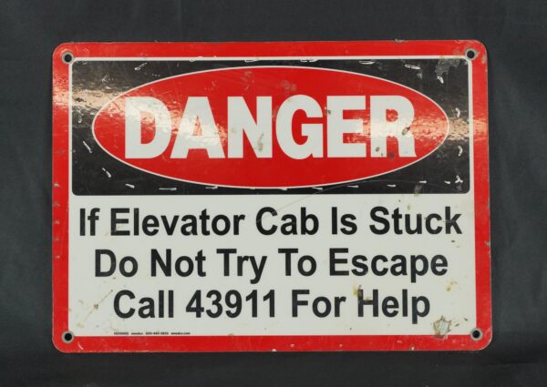 Industrial safety wall sign with a red and black danger notice, four mounting holes, and visible surface wear.