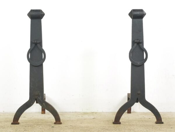 Pair of antique Arts & Crafts wrought iron andirons shown as a matching pair with front rings, curved feet, and visible surface wear.
