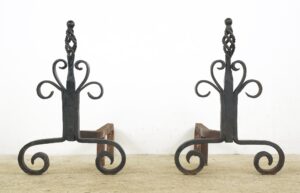 Pair of wrought iron andirons with twisted cage finials and scrollwork feet, shown as a matching pair.