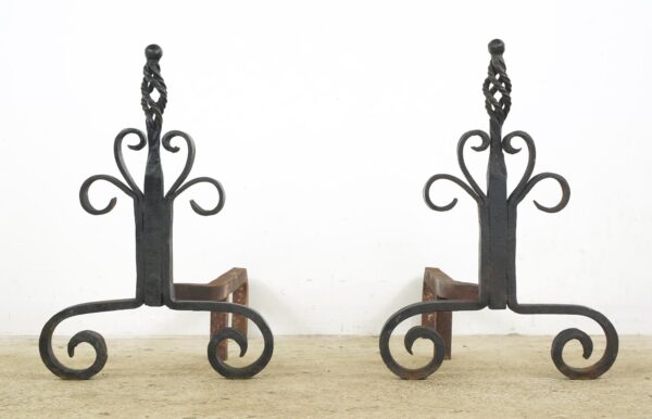 Pair of wrought iron andirons with twisted cage finials and scrollwork feet, shown as a matching pair.