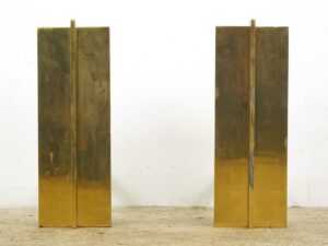 Pair of polished brass fireplace andirons shown as two tall rectangular panels with visible surface wear.