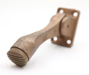 Vintage gold-painted cast iron kickdown door stop with a worn rubber bottom and mounting plate shown at an angle.