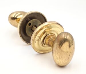 Polished brass passage door knob set with oval knobs, concentric rosettes, and a spindle, shown in close-up with visible surface wear.