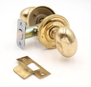 Reclaimed polished brass passage door knob set with oval knobs, concentric rosettes, a mortise, and a strike plate, shown with surface wear and the original mounting screws absent.