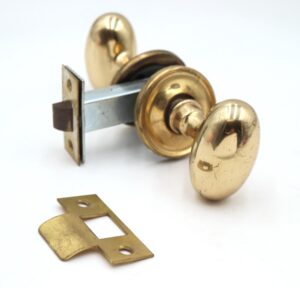 Reclaimed polished brass passage door knob set with oval knobs, concentric rosettes, a mortise, and a strike plate shown in a product photo.