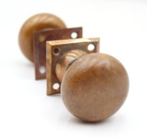 Close-up of a vintage brass passage door knob set with visible surface wear and a square back plate behind it.