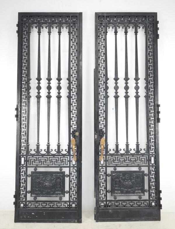 French wrought iron double entry doors with Greek key frames, ornate relief panels, and attached brass pulls shown closed side by side.