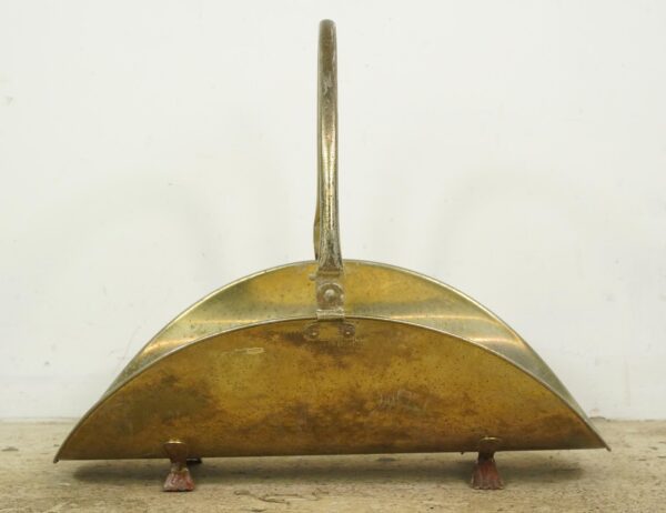 Vintage brass-plated steel log holder with a curved scoop, overhead swing handle, and claw feet, shown with visible surface wear and rust.