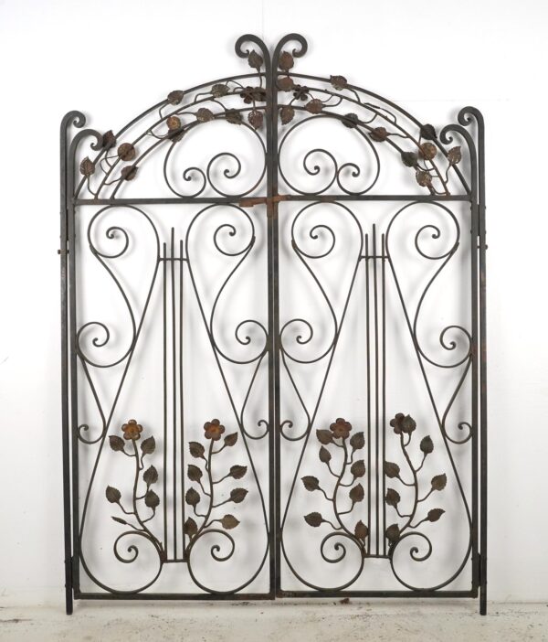 Wrought iron double garden gates with an arched header, scrollwork, and ivy vine details.