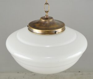 Schoolhouse pendant light with a white milk glass globe and antique brass chain fitter, shown in a close-up view of the upper section.