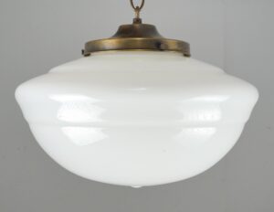 Schoolhouse pendant light with a white milk glass globe and antique brass fitter, shown in a close front view.